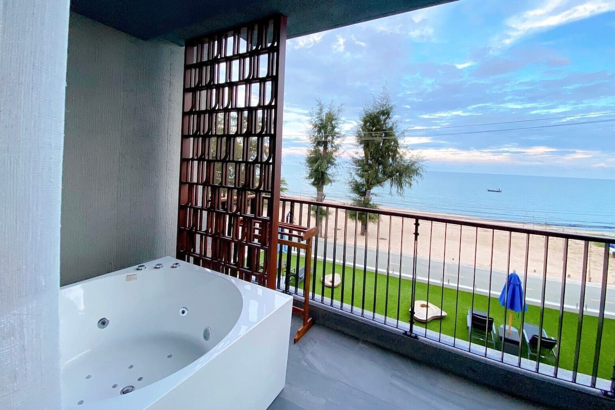 Un balcón con una bañera blanca, vista a la playa y una valla.