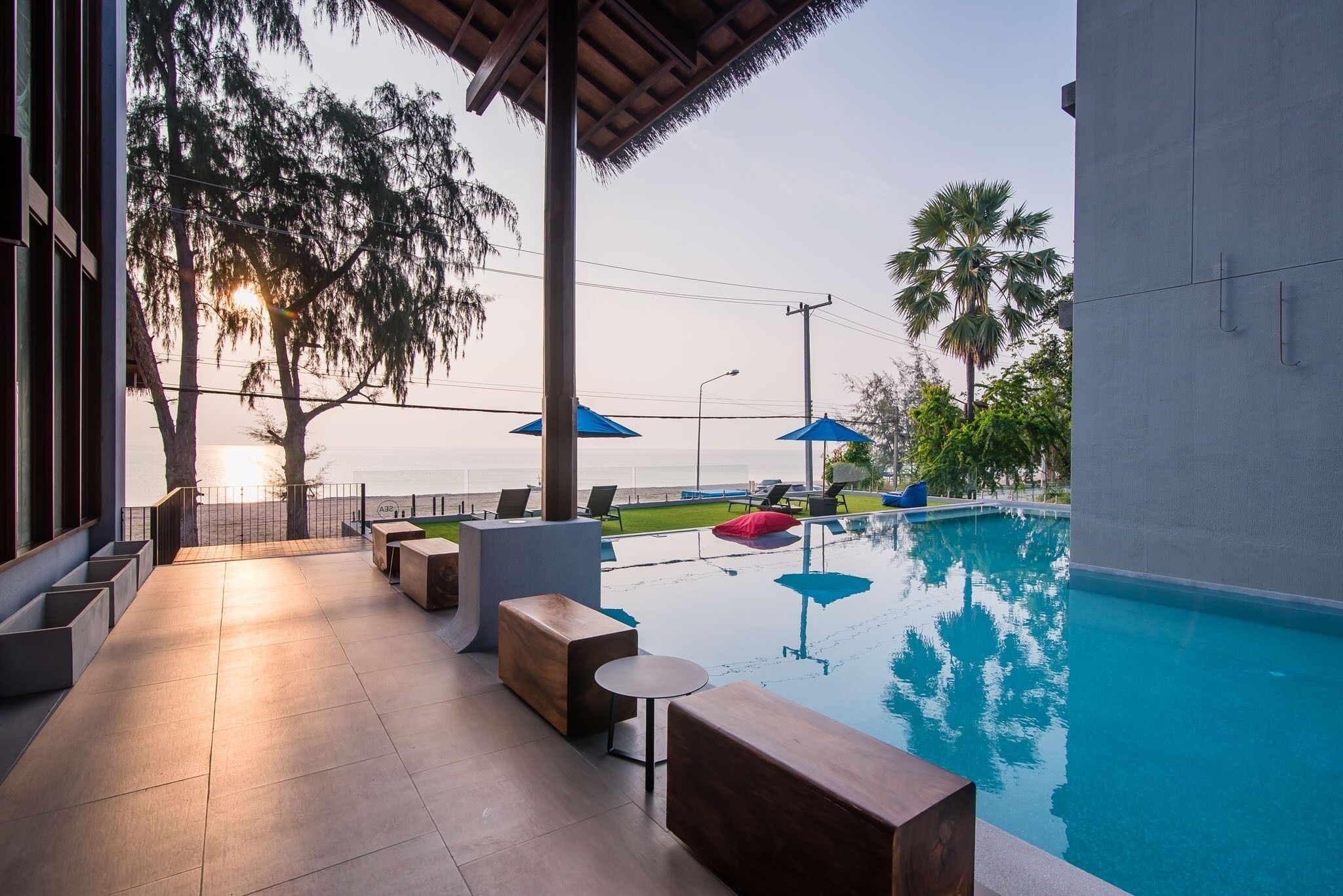 A pool area with lounge chairs and umbrellas, a covered seating area, and a view of the sea.