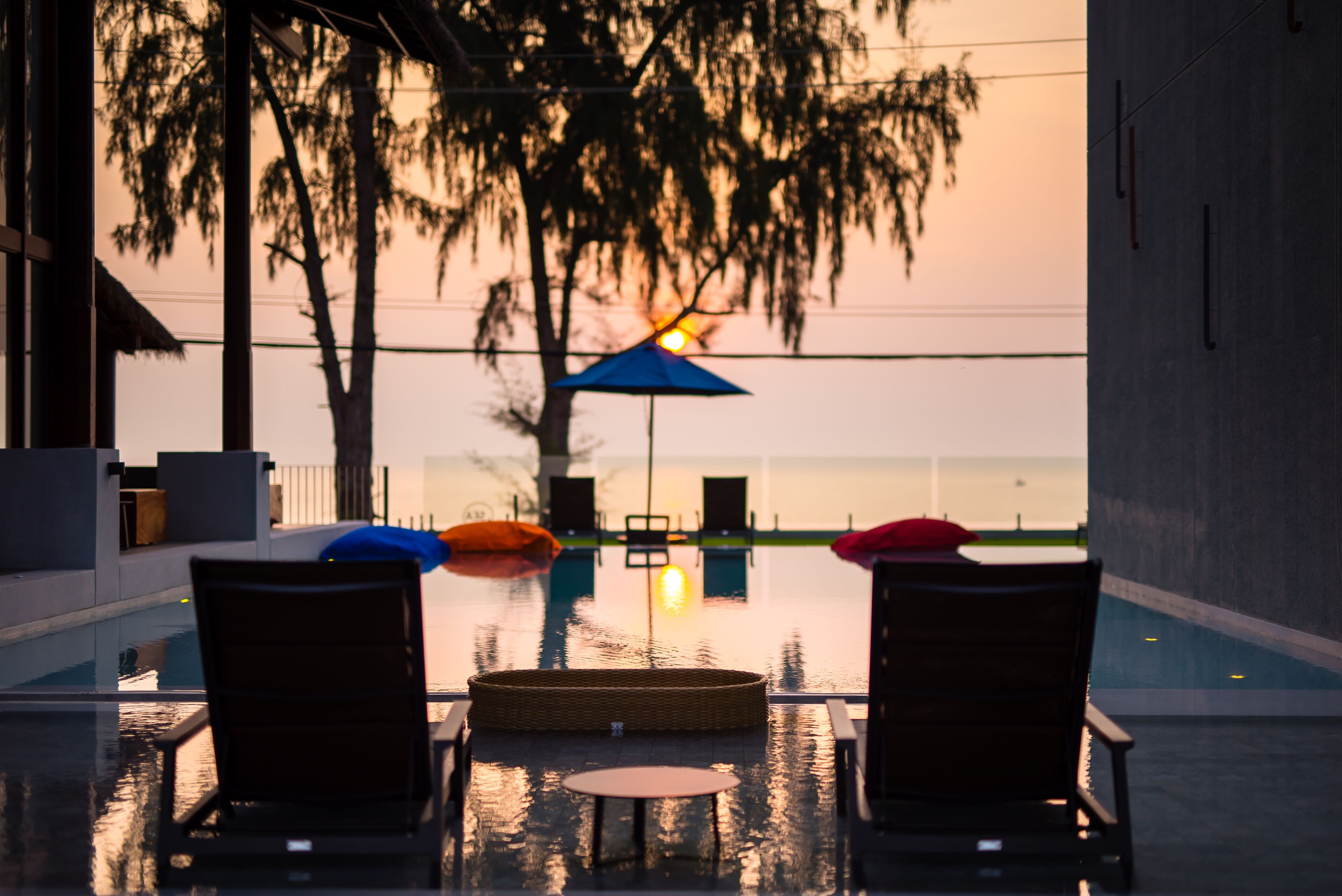 A poolside area with lounge chairs and a table, overlooking a body of water and trees.