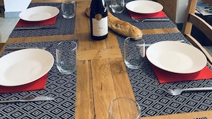 Una mesa de comedor dispuesta con platos, vasos y una botella de vino, con una cocina al fondo.