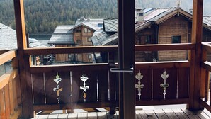 Un balcón de madera con puerta de cristal que ofrece vistas a una montaña boscosa y edificios tradicionales de madera.