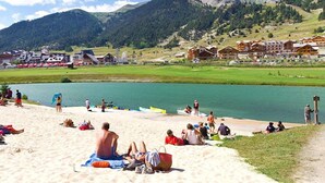 Una playa con gente tomando el sol y nadando, rodeada de montañas y un lago.