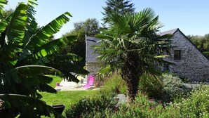A stone house with a garden, including a palm tree and banana plants. - Holiday Home in Guerlesquin near Lake (Guerlesquin)