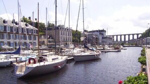 A marina with several sailboats docked, a bridge in the background, and buildings along the waterfront. - Holiday Home in Guerlesquin near Lake (Guerlesquin)