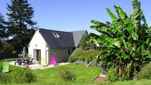 A house with a stone exterior, a sloped roof, and a small patio with outdoor furniture. - Holiday Home in Guerlesquin near Lake (Guerlesquin)