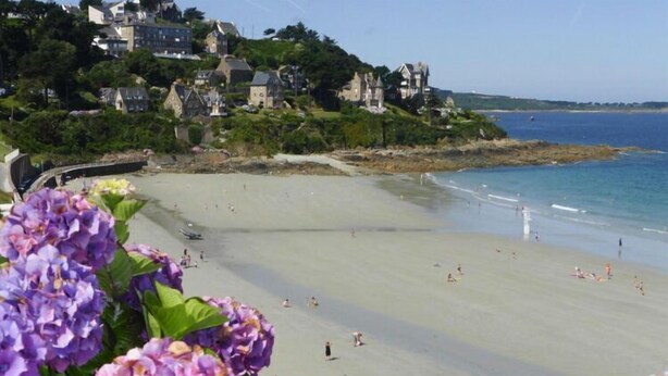 A beach with people, a pier, and buildings in the background. - Holiday Home in Guerlesquin near Lake (Guerlesquin)