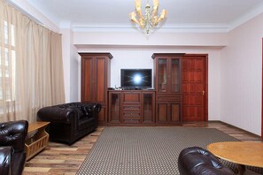 A living room with a dark brown leather sofa, a wooden coffee table, a TV on a stand, and a patterned rug.