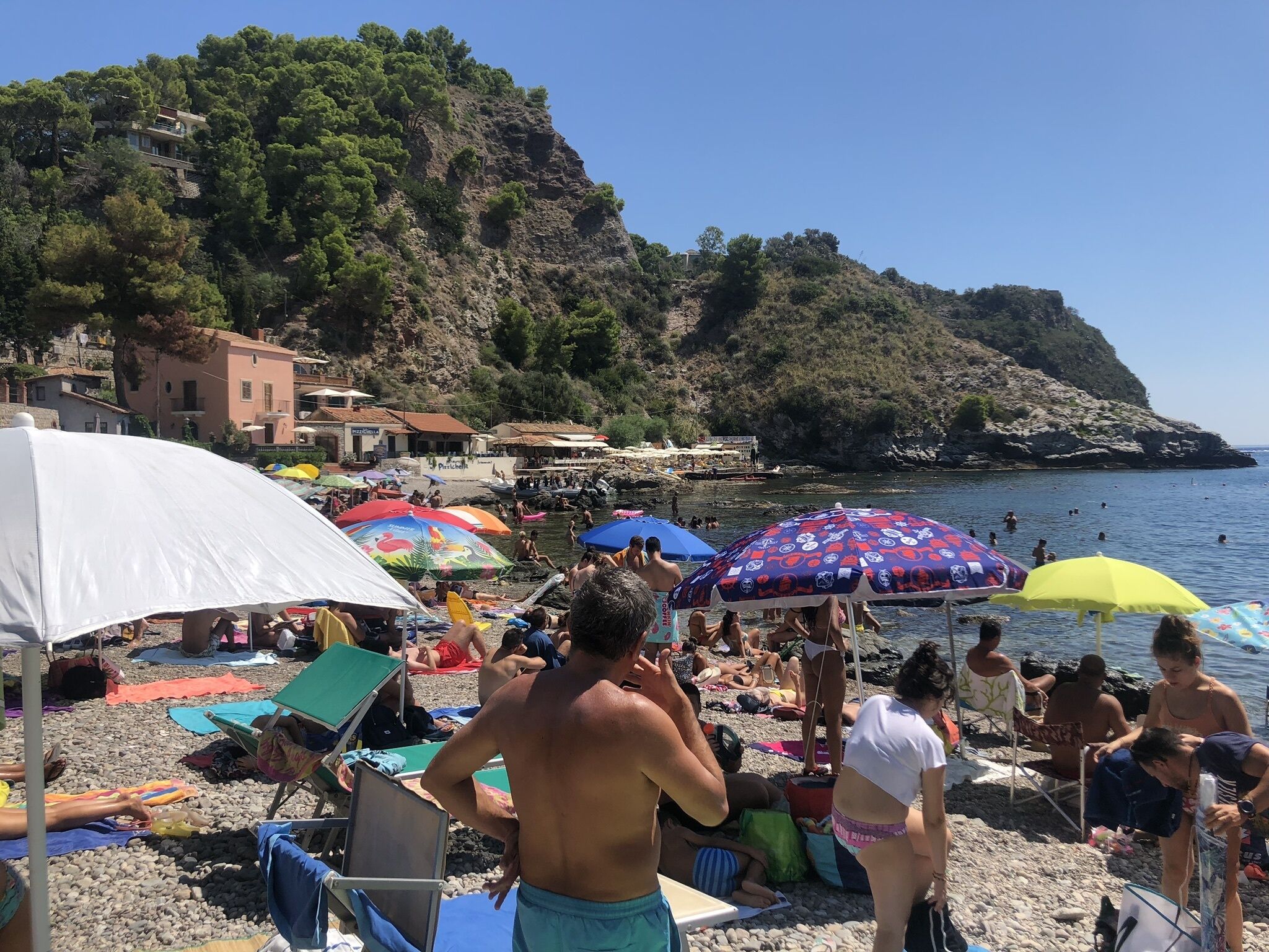 Ein voller Strand mit badenden und sonnenden Menschen, umgeben von bunten Sonnenschirmen und Liegestühlen.