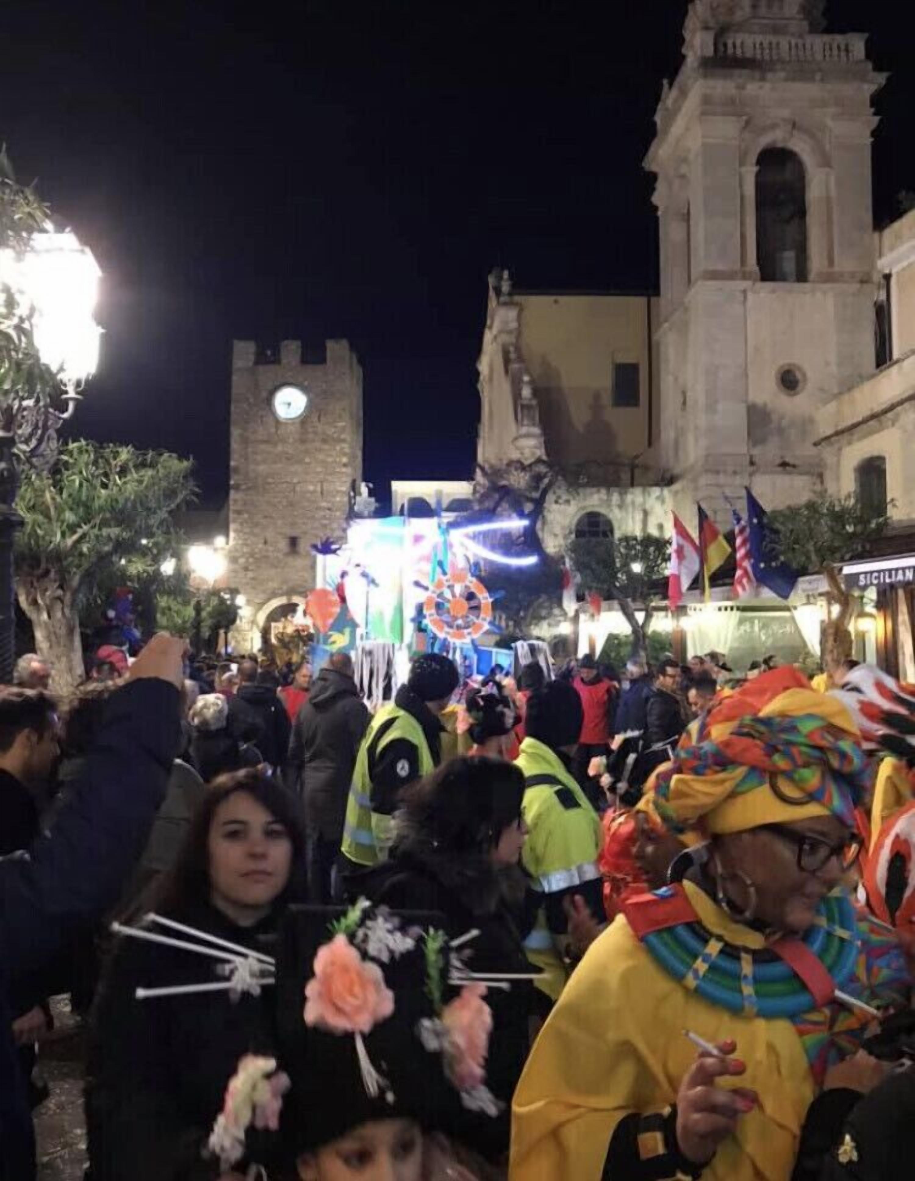 A crowded street scene at night with historical buildings and flags.