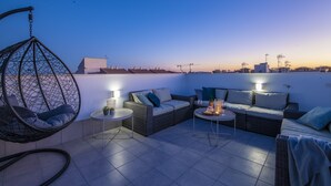 Terraza en la azotea con muebles de mimbre, dos mesas con lámparas y una silla colgante.