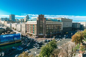 A large building with multiple floors and a central tower, surrounded by a busy street with cars and pedestrians. - Apartments Kreshchatik 27-28 (Kyiv)