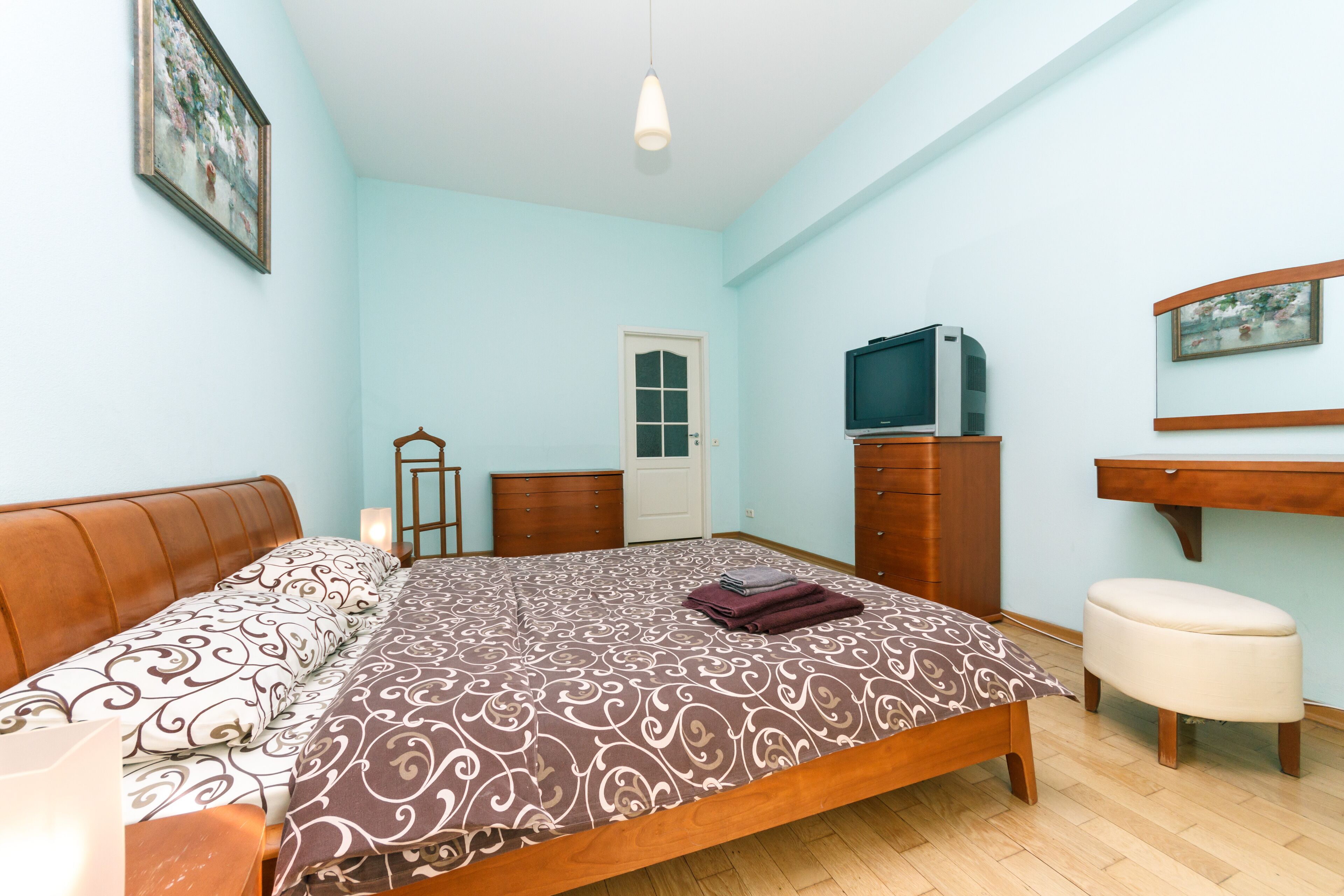 A bedroom with a bed, a dresser, a television, and a door.