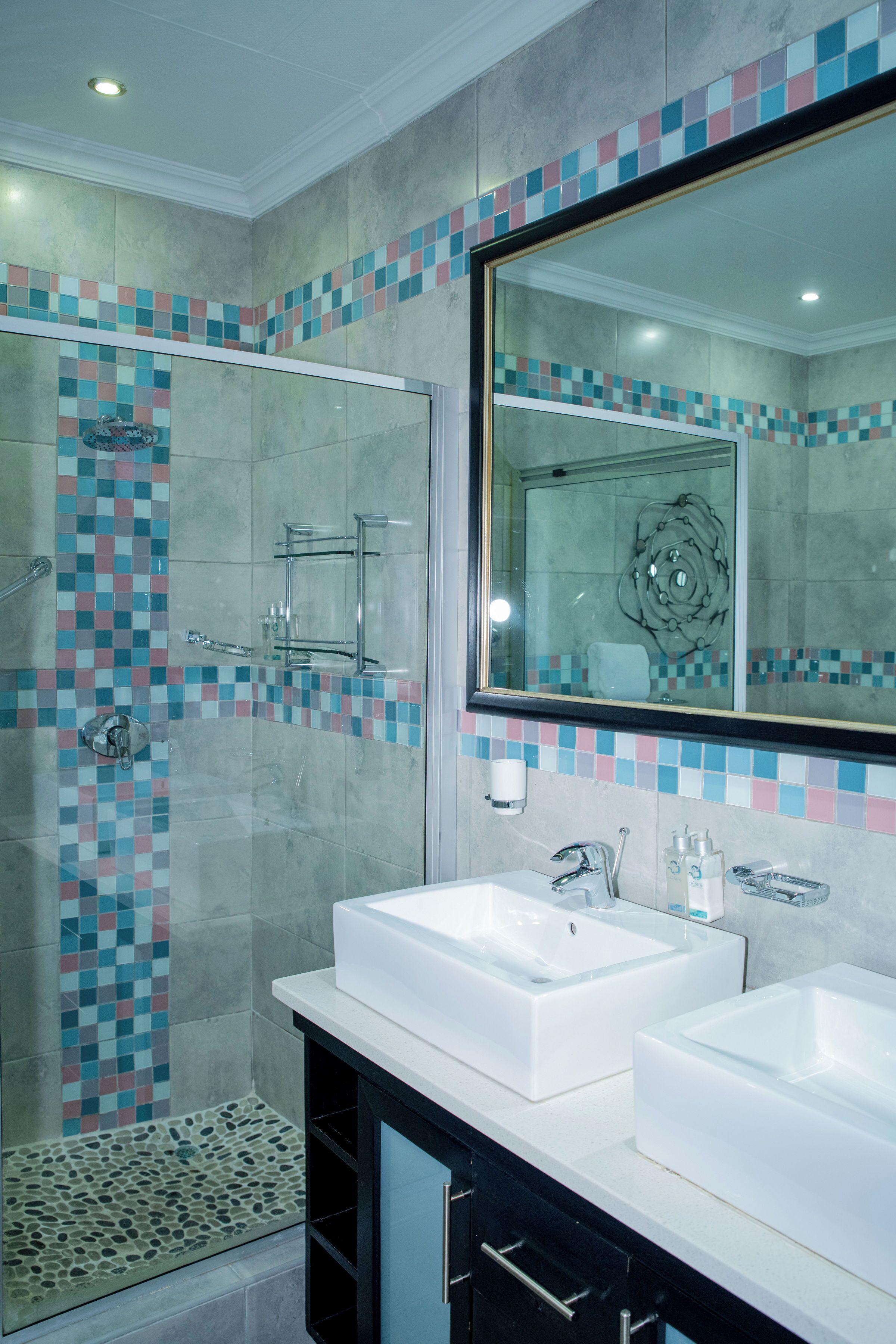 Un bagno moderno con due lavabi, cabina doccia in vetro e schienale rivestito in piastrelle.