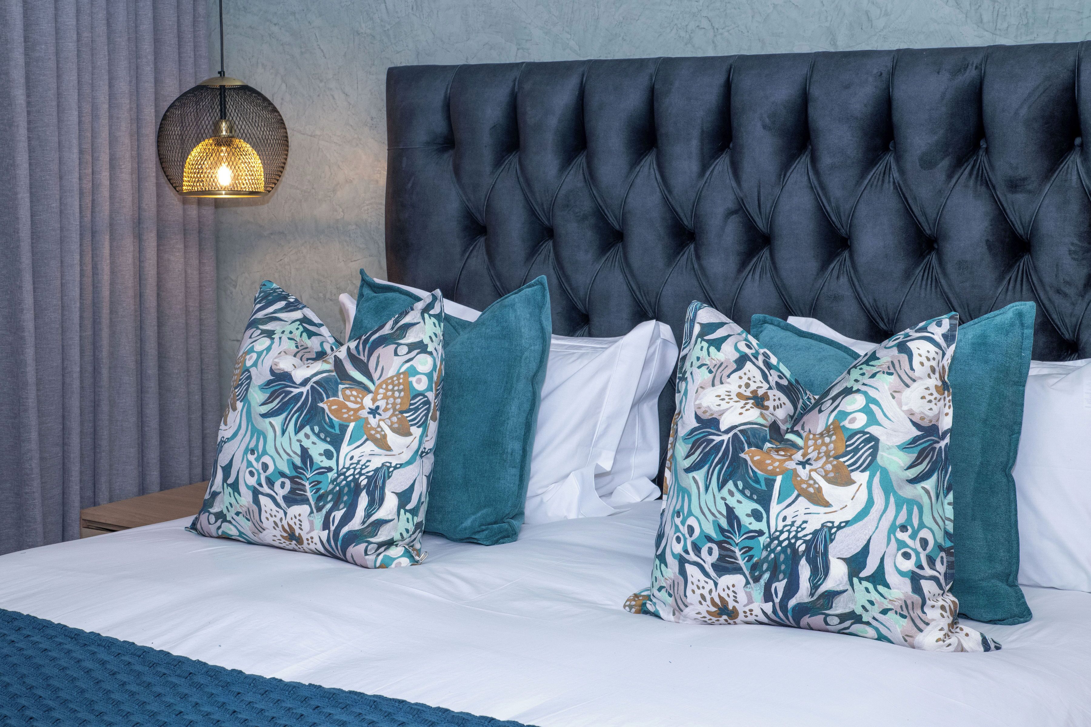 A bed with a tufted headboard, patterned pillows, and a textured throw blanket.