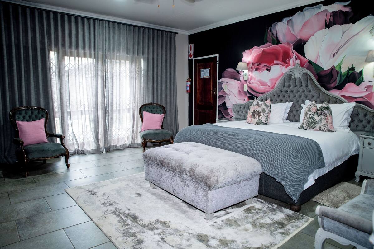 A bedroom with a large bed, two chairs, a rug, and a floral mural on the wall.