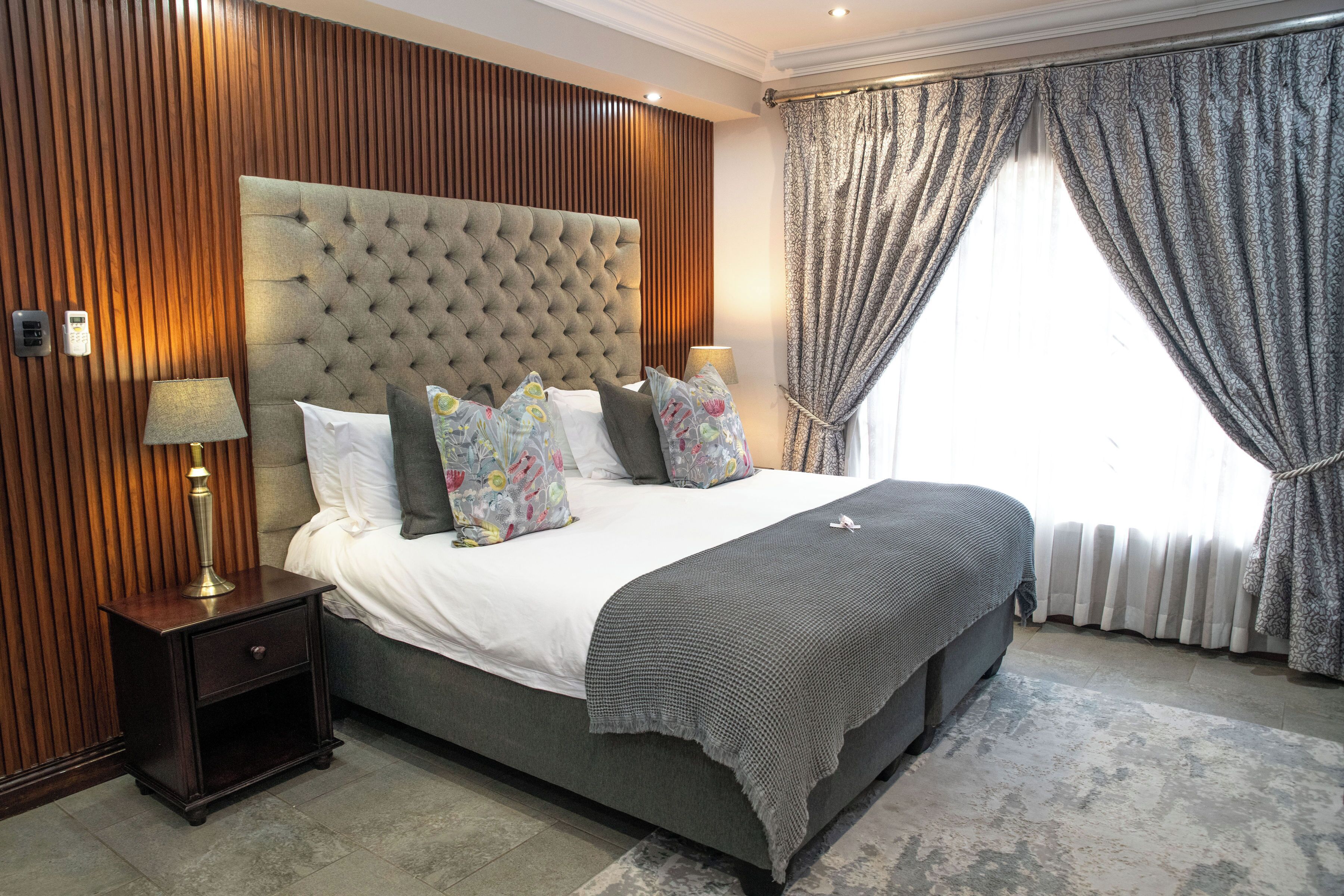 A bedroom with a tufted headboard, a large bed with multiple pillows, a bedside table with a lamp, and a window with curtains.