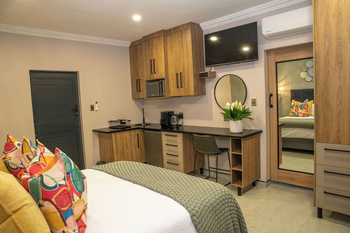 A bedroom with a bed, a desk, a chair, a microwave, a television, and a wardrobe.