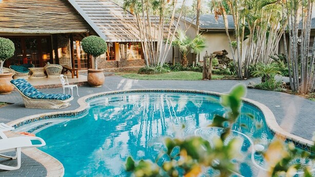 Una piscina con sillones de descanso y un edificio pequeño al fondo.