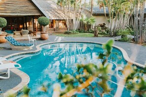 Piscina com espreguiçadeiras e um pequeno edifício ao fundo.