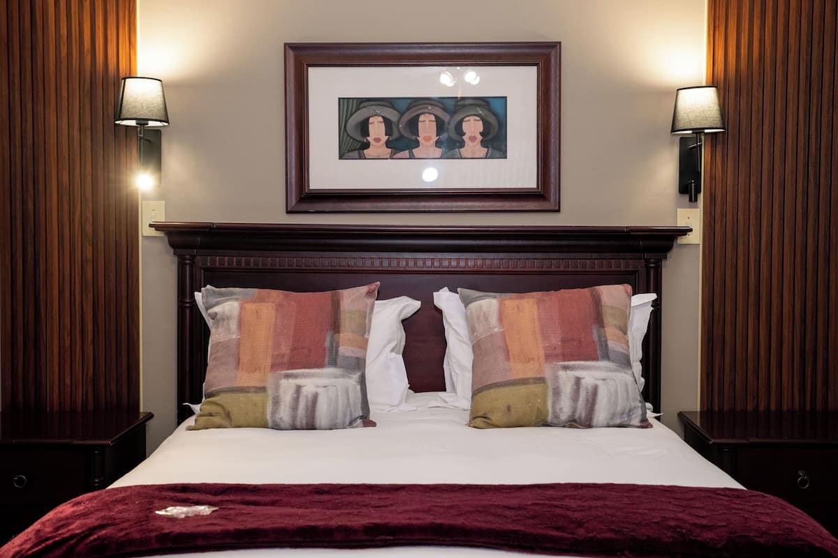 A neatly made bed with a red blanket, two decorative pillows, and a framed artwork above it.
