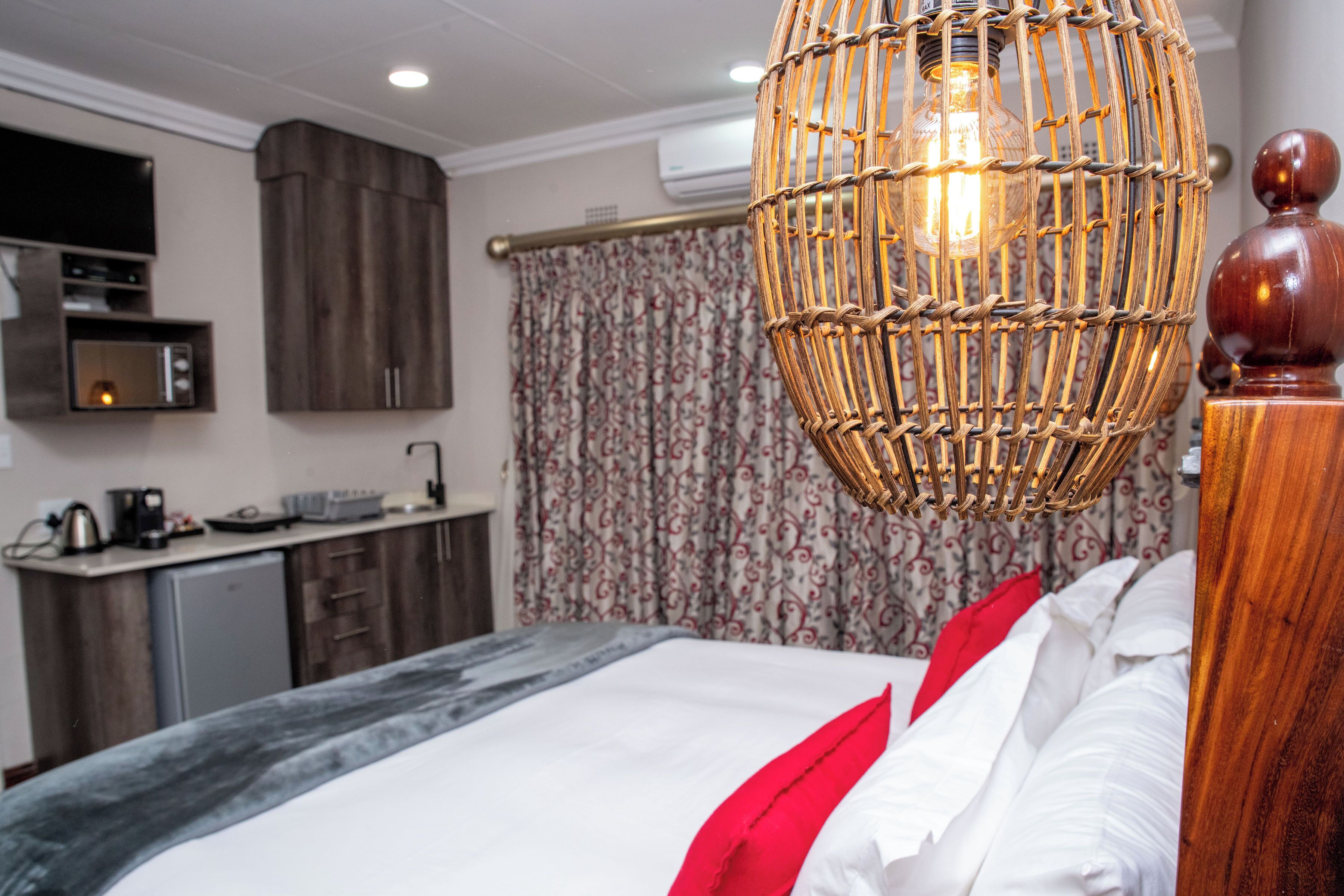 A hotel room with a bed, a bedside table, a hanging light fixture, a wardrobe, a microwave, a coffee maker, and a curtain with a floral pattern.