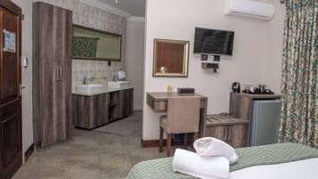 Habitación de hotel con cama, escritorio, silla, televisor, espejo, lavamanos y armario.