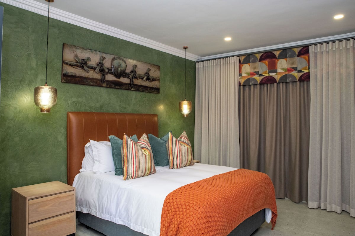 A bedroom with a bed, a nightstand, a painting on the wall, and a window with curtains.