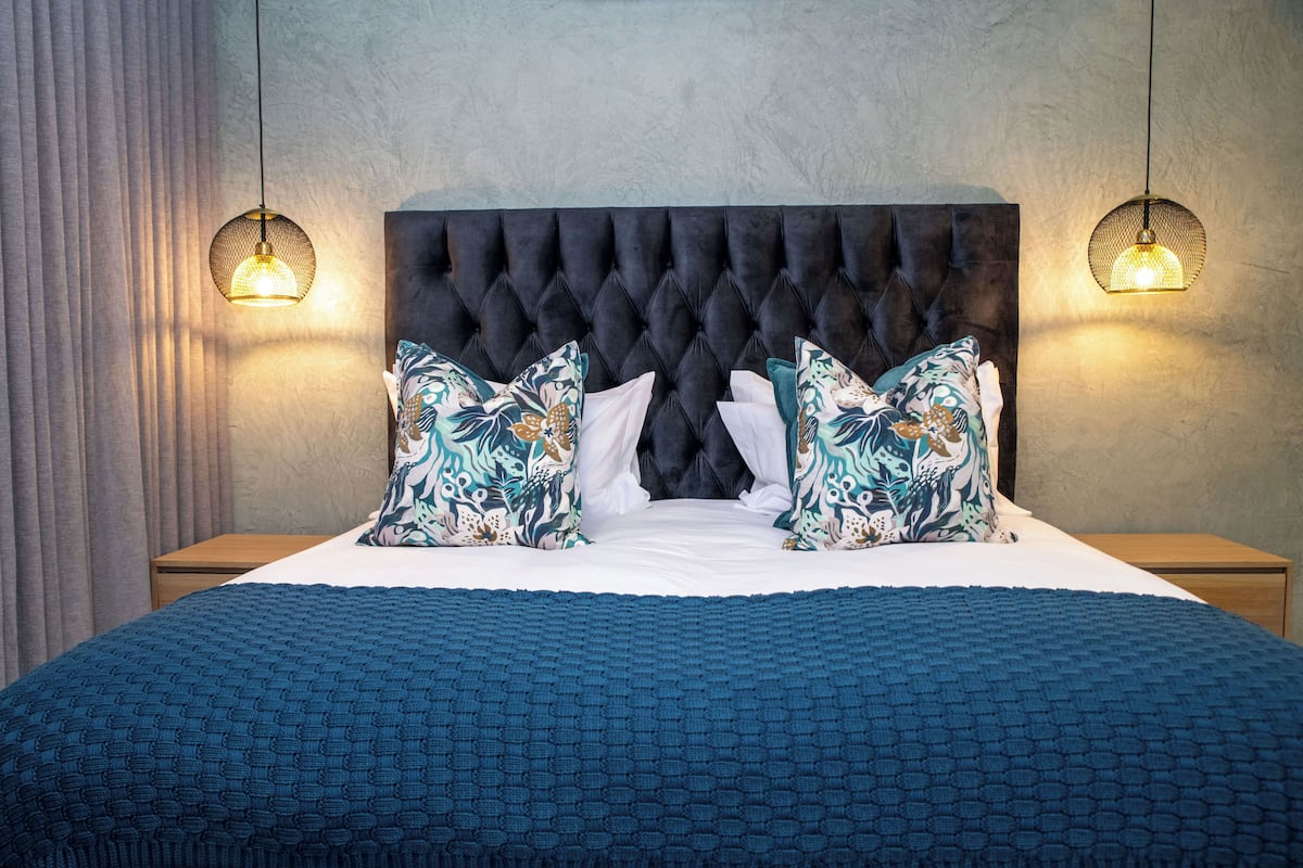 A neatly made bed with a tufted headboard, two bedside lamps, and a blue textured bedspread.