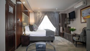 Una habitación de hotel con cama, escritorio, silla, televisor y ventana con cortinas.