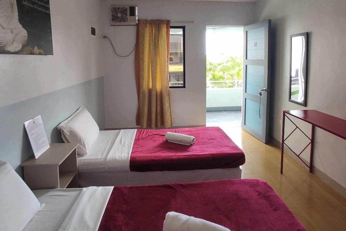 Una habitación de hotel con dos camas, una ventana con cortinas, una puerta y una mesita.