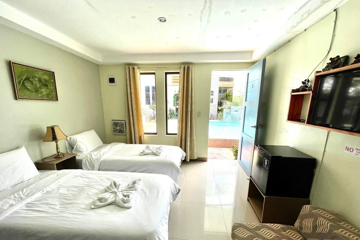 A hotel room with two beds, a TV, a desk, and a view of the outside.