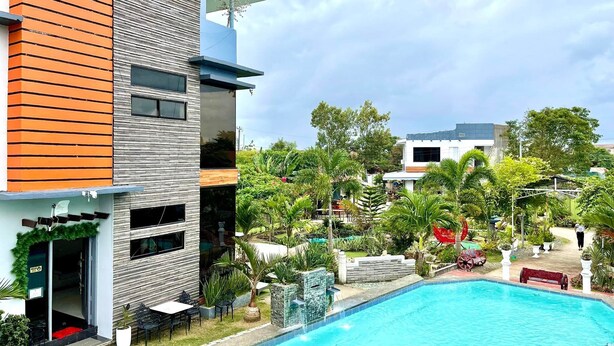 A modern building with a swimming pool, surrounded by lush greenery and palm trees. - Little Rock Cebu (Lapu-Lapu)