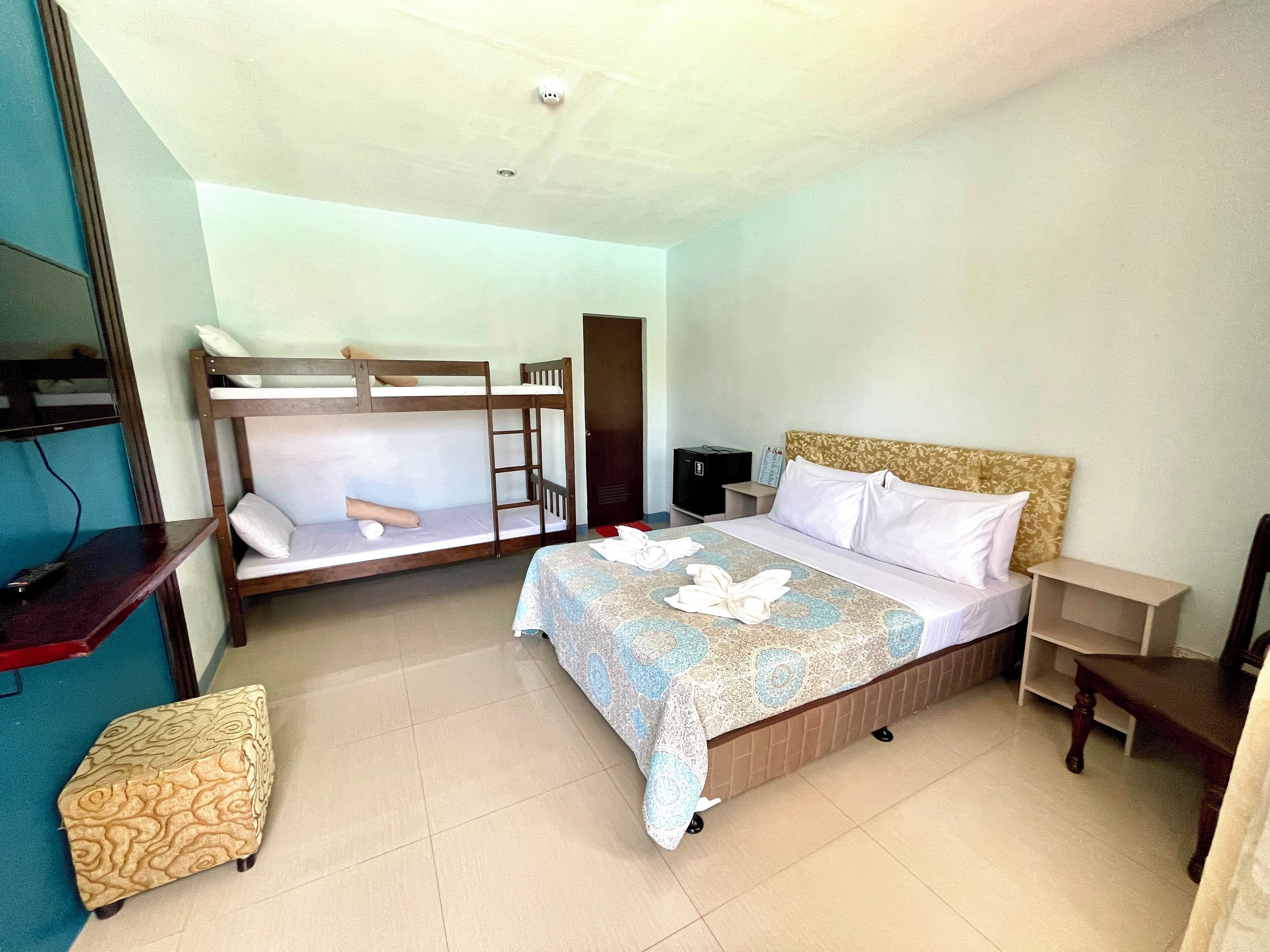 A hotel room with a bunk bed, a single bed, a desk, and a television.