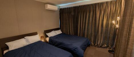 A hotel room with two beds, a ceiling light, an air conditioning unit, and a curtain.