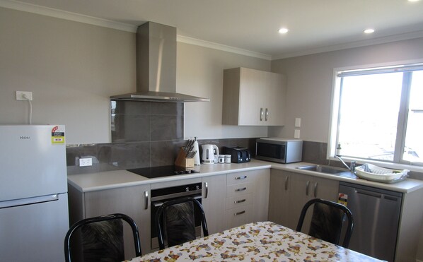 A compact kitchen with a refrigerator, stove, microwave, and a window providing natural light. - Jaw Dropping Views, Taupo View Loft in stunning Wharewaka. (Wharewaka)