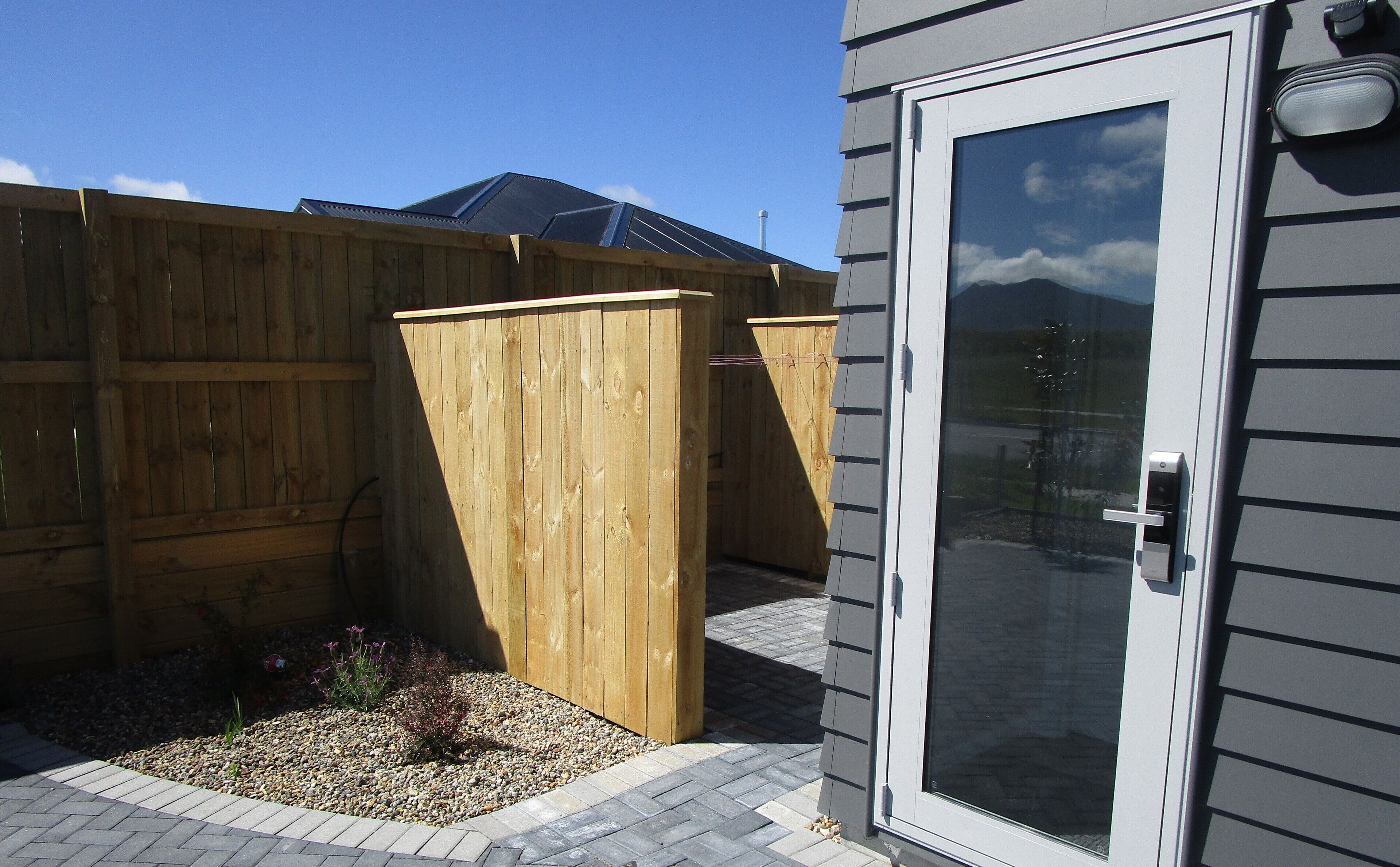 A wooden fence, a door with a window, and a paved patio area.