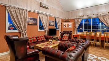 A living room with leather sofas, a wooden coffee table, and a TV. There are curtains, a fireplace, and a dining area with a table and chairs.