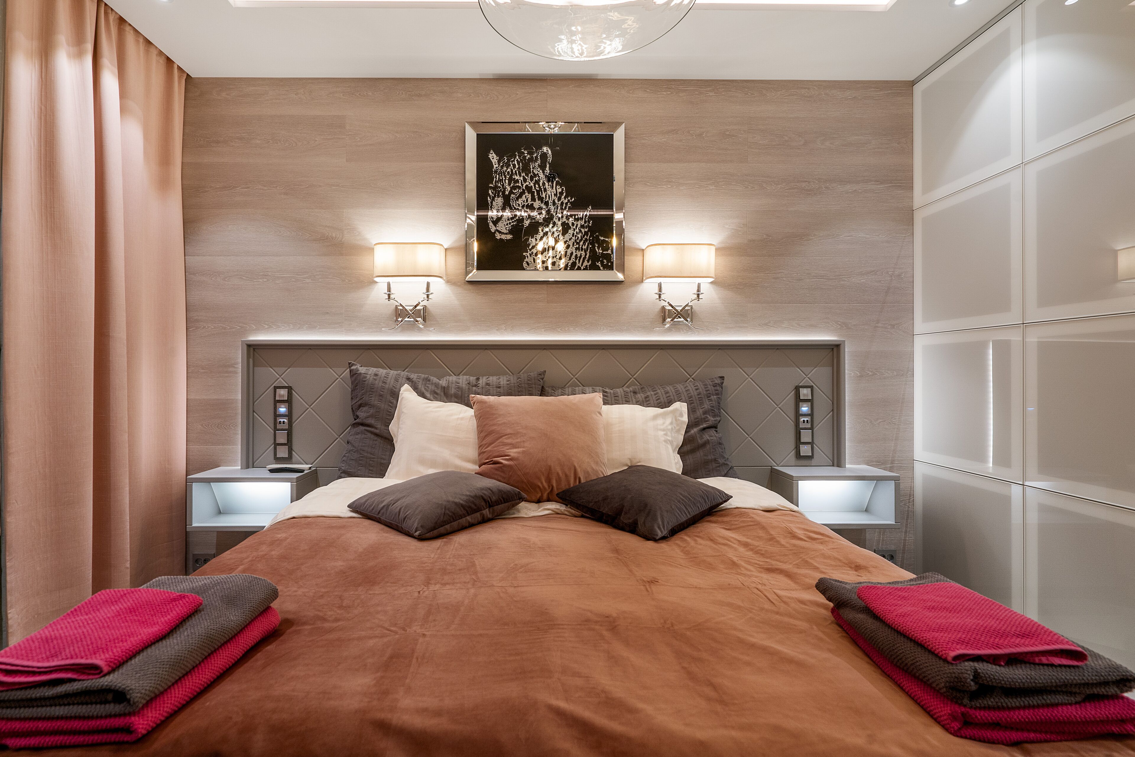 A modern hotel room with a large bed, two bedside lamps, a wall-mounted artwork, and a built-in wardrobe.