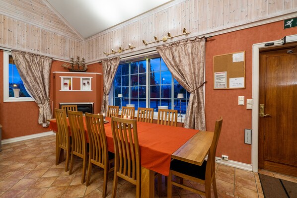 A dining room with a large table set for eight, wooden chairs, a fireplace, and a window with curtains.