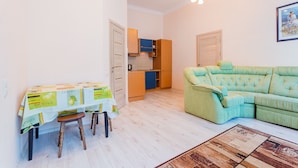 A compact living space with a dining table, a green sofa, and a kitchen area. - Apartment Kreschatik Luteranskaya (Kyiv)