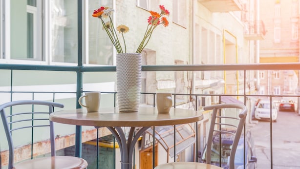 A balcony with a round table and two chairs, a vase with flowers, and a view of a street with parked cars. - Apartment Kreschatik Luteranskaya (Kyiv)