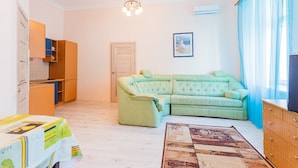 A living room with a sectional sofa, a wooden cabinet, a table with a tablecloth, a chandelier, and a patterned rug. - Apartment Kreschatik Luteranskaya (Kyiv)