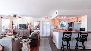 Una cocina moderna con una isla central, armarios de madera y un comedor con dos taburetes de bar.