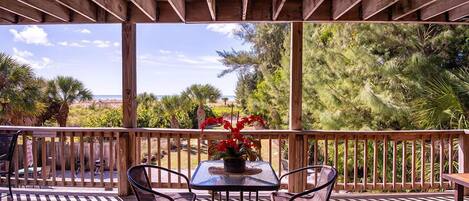 An outdoor patio with a wooden pergola, a table with chairs, and a view of the ocean and trees.
