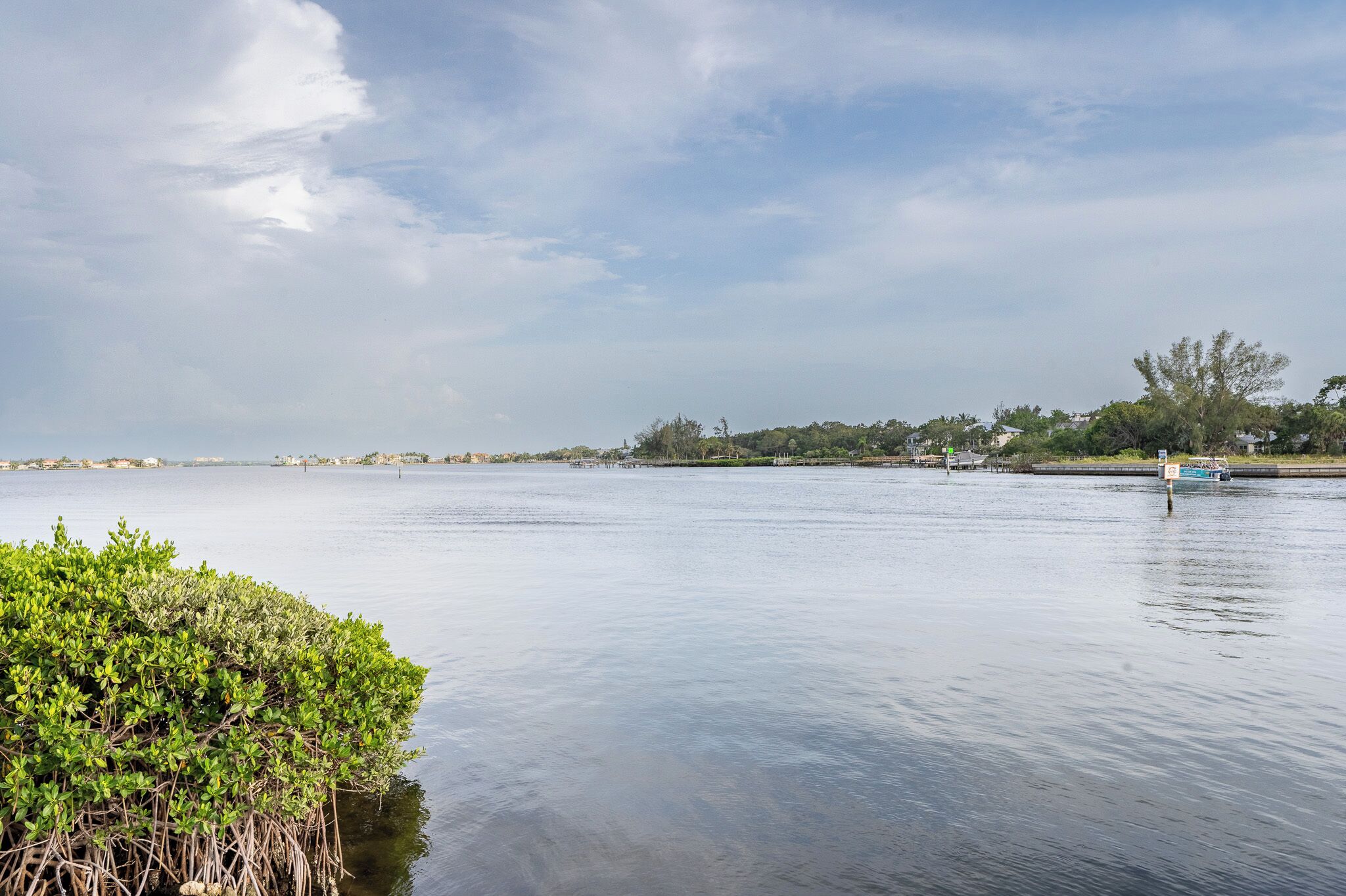 A calm river with a dock and greenery on the left.