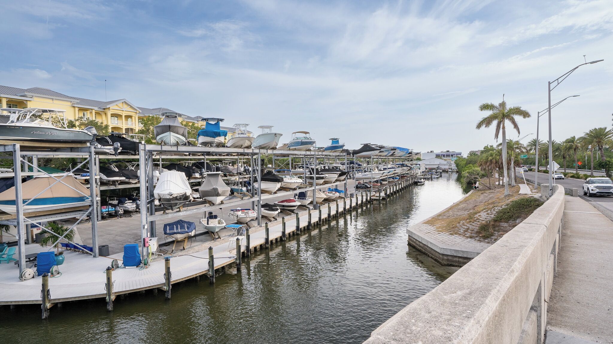 A marina with boats docked along a narrow waterway, connected to a docked area with covered seating and a small building.