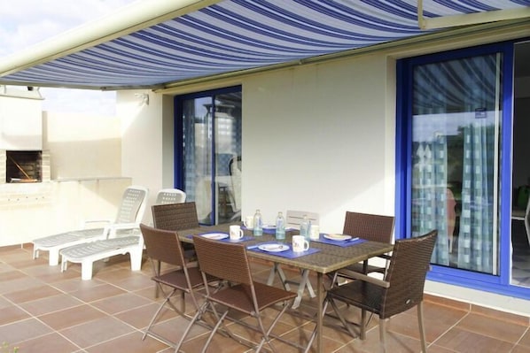 An outdoor patio with a table set for four, surrounded by wicker chairs, and a striped awning overhead.