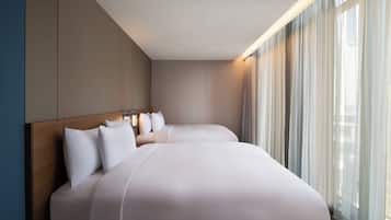 A hotel room with two beds, a wooden headboard, and a large window with sheer curtains.