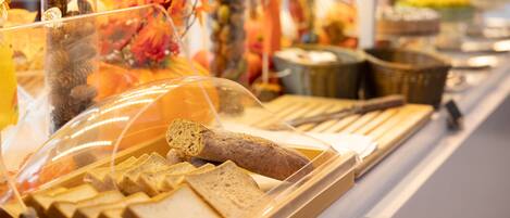 A buffet with various food items, including bread and pastries, displayed in a clear plastic cover.