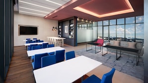 Une salle de conférence moderne, dotée de tables blanches, de chaises bleues, d’un canapé et d’une grande fenêtre donnant sur la ville.